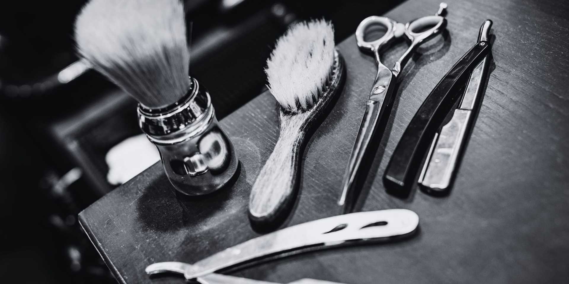 Vintage barber tools, including razors, scissors, brushes, and a shaving brush on a wooden surface.