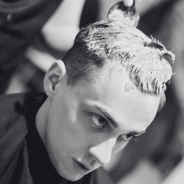 Man getting hair dyed, seen in black and white, at a salon.