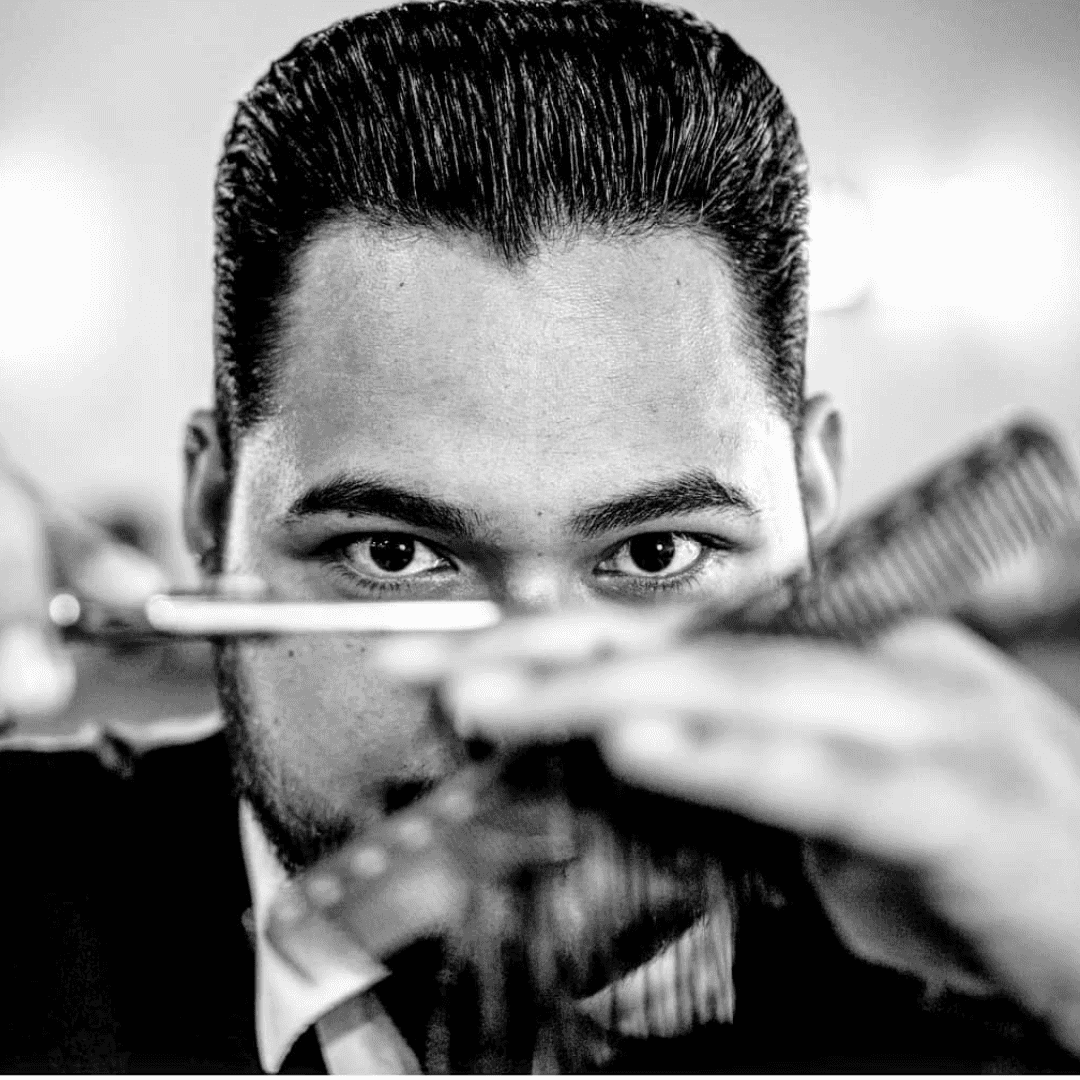 Barber concentrating while cutting hair with scissors and a comb, black and white photo.